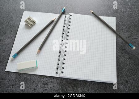 Working desktop with a blank open spiral notebook, pencils, sharpener and eraser on a dark gray table, mock up with copy space, selected focus, narrow Stock Photo