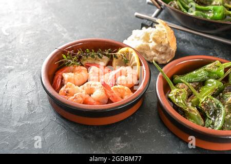 Spanish tapas in traditional bowls, fried pimientos or padron peppers and shrimps with lemon and herbs on a gray slate background, copy space, selecte Stock Photo