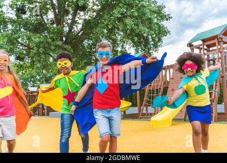 Multiracial group of young schooler wearing superhero costumes and having fun outdoors Stock Photo