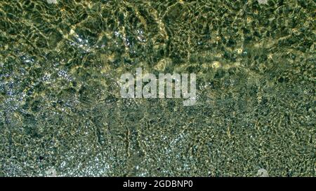 Azure sea water over yellow sandy bottom with small pebbles, sparkling in sun with bright reflections and stars, forms an attractive pattern with ligh Stock Photo