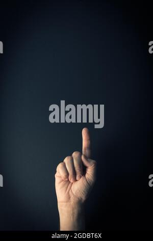 Dramatic colour image of male hand demonstrating sign language number one against dark background with empty copy space for editors Stock Photo