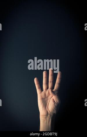 Dramatic colour image of male hand demonstrating sign language number four against dark background with empty copy space for editors Stock Photo