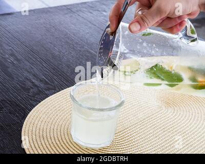 homemade lemonade is pouring from glass jug with filter mesh into glass Stock Photo