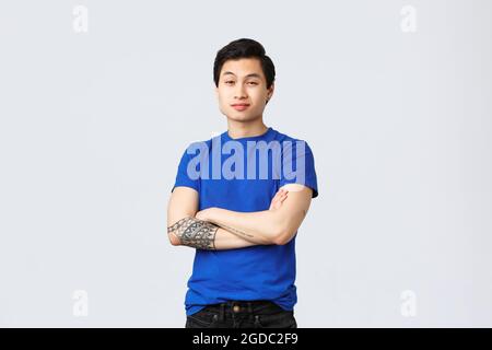 People different emotions, lifestyle and casual concept. Handsome, confident young asian guy in blue t-shirt, cross arms chest and staring at camera Stock Photo