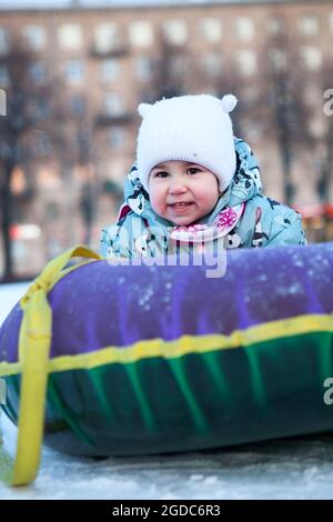 Smiling and happy baby with snowing tube, sliding on snowy slope. Caucasian child Stock Photo