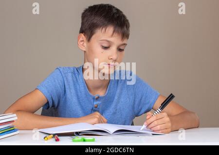Boy hand holding pen in left hand and writing in a notebook, doing homework. Left Handers Day Stock Photo