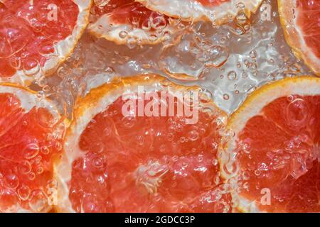 Grapefruit close-up in liquid with bubbles. Slice of blood red ripe grapefruit in water. Close-up fresh slices of red grapefruit on white background Stock Photo