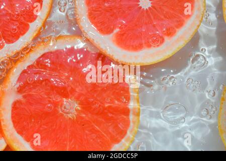 Grapefruit close-up in liquid with bubbles. Slice of blood red ripe grapefruit in water. Close-up fresh slices of red grapefruit on white background Stock Photo