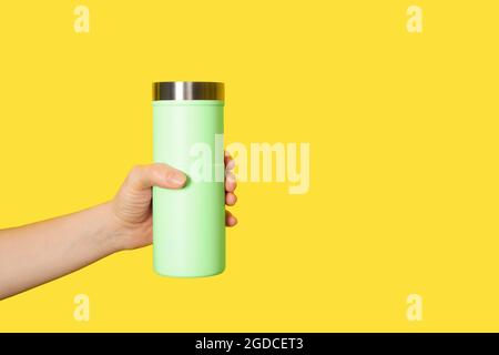 Hand holds light yellow travel mug isolated on white background. Thermo cup or tumbler in female hand. Banner with copy space. Stock Photo