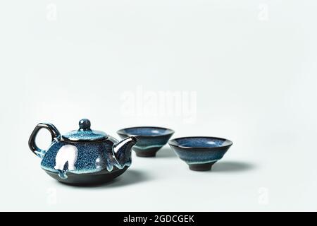 Green tea in a dark blue clay teapot and two small cups on pastel background. Creative minimalist tea ceremony concept. Copy space. Stock Photo
