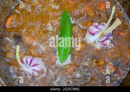 Hot pepper and garlic heads in boiling water, covering sliced carrots and pieces of meat in a cauldron in the process of cooking pilaf on a traditiona Stock Photo