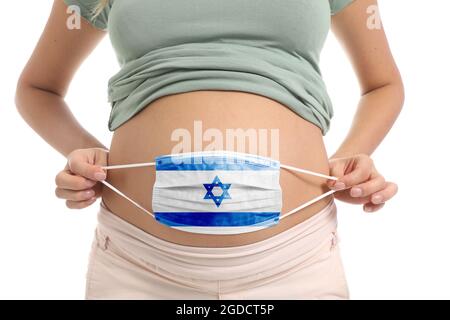 Pregnant woman holding medical mask with painted Israeli flag on white background Stock Photo