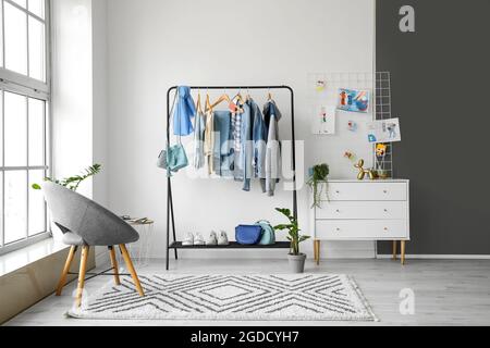 Rack with stylish clothes, chair and chest of drawers in room Stock Photo