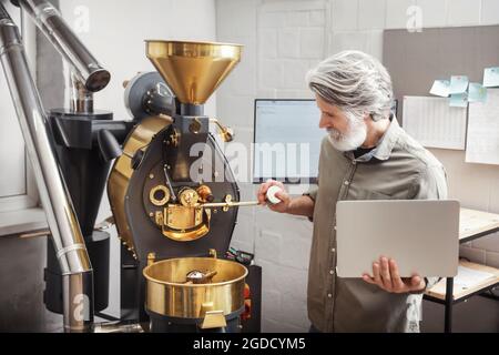 Senior man with laptop using modern coffee roaster Stock Photo
