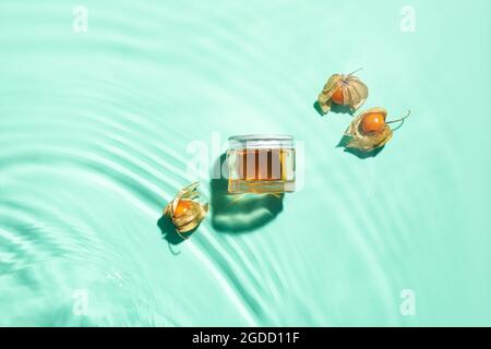Jar of cream and physalis in water on color background Stock Photo