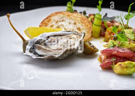 Oyster on a white plate with lemon, crouton and tartare Stock Photo