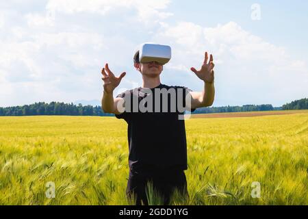 Man using virtual reality glasses outside in nature on a wheat farming field. Stock Photo