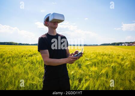Man flying a drone with virtual reality glasses outside in nature on a wheat farming field. Stock Photo