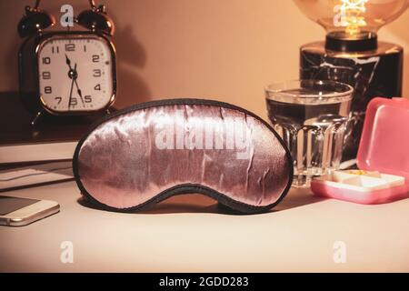 Sleeping mask with pills and glass of water on light background Stock Photo