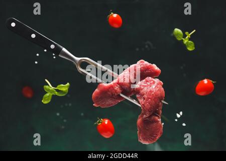 Carving fork with raw beef meat slices on dark background Stock Photo