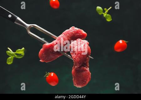 Carving fork with raw beef meat slices on dark background Stock Photo