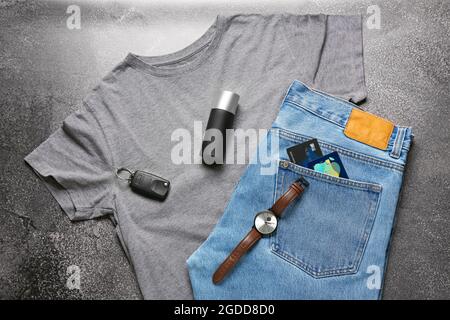 Composition with stylish t-shirt, jeans, car key and wrist watch on dark background Stock Photo