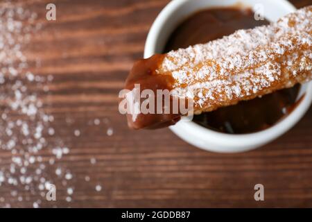 Tasty churro and melted chocolate sauce in bowl on wooden background, closeup Stock Photo