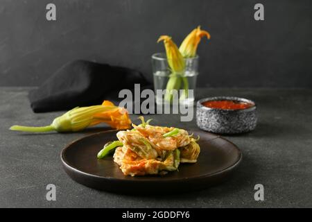 Plate with fried zucchini flowers and sauce on dark background, closeup Stock Photo