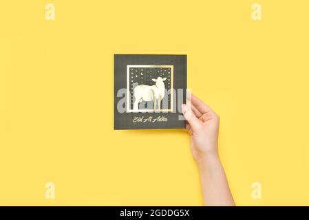 Female hand with greeting card for Eid al-Adha (Feast of the Sacrifice) on color background Stock Photo