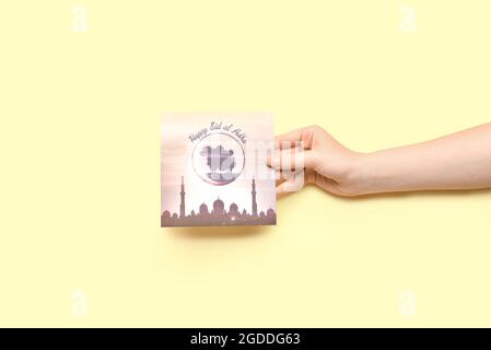 Female hand with greeting card for Eid al-Adha (Feast of the Sacrifice) on light background Stock Photo