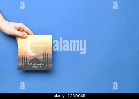 Female hand with greeting card for Eid al-Adha (Feast of the Sacrifice) on color background Stock Photo