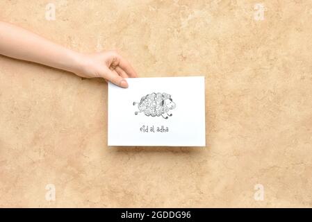 Female hand with greeting card for Eid al-Adha (Feast of the Sacrifice) on color background Stock Photo