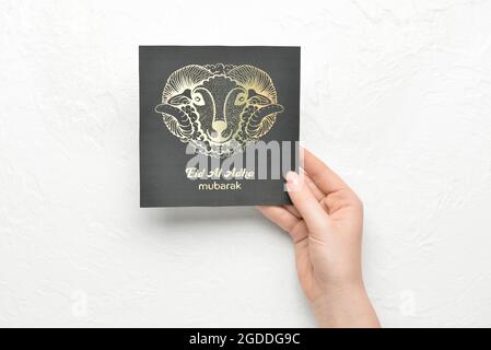 Female hand with greeting card for Eid al-Adha (Feast of the Sacrifice) on white background Stock Photo