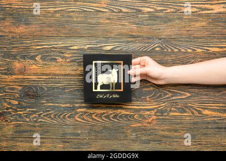 Female hand with greeting card for Eid al-Adha (Feast of the Sacrifice) on wooden background Stock Photo