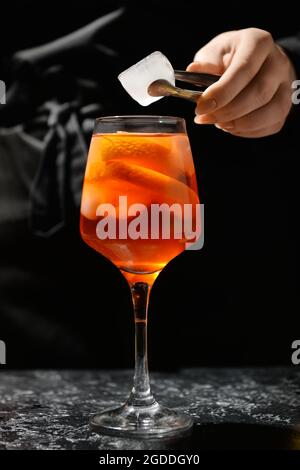 Female bartender preparing tasty aperol spritz cocktail on dark background, closeup Stock Photo