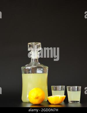 Lemon liqueur in two glasses and a glass bottle on a black background, ripe cut citrus next to it. Close-up. Stock Photo