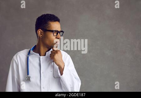 Male african american doctor confused about idea thinking looking aside Stock Photo