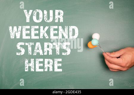 Your weekend starts here. Miniature balloons in a man's hands on a green chalk board. Stock Photo