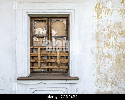 boarded up window with broken glass on weathered plaster wall of abandoned old building Stock Photo