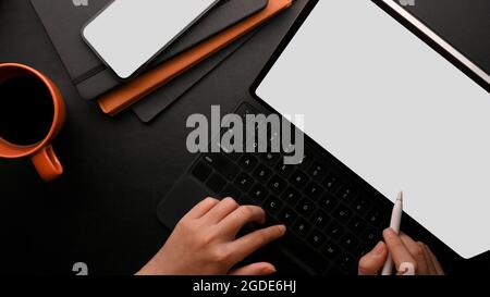 Modern office workspace top view, hands working on black tablet with keyboard, white screen mobile phone mockup, orange coffee mug with black coffee, Stock Photo