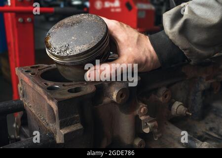 An auto mechanic shows a worn out engine piston with a deformation on the head Stock Photo
