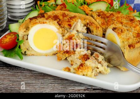 Scotch egg quiche with shortcrust pastry and whole egg encased in pork sausage meat with fresh salad Stock Photo