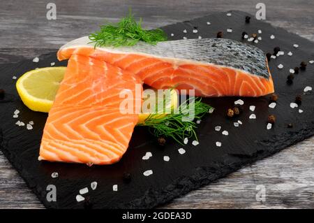 Two fresh raw salmon fillets with dill herb garnish and lemon slices on a slate serving board Stock Photo