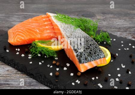 Two fresh raw salmon fillets with dill herb garnish and lemon slices on a slate serving board Stock Photo