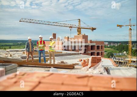 Builders in hardhats conversing with an engineer on the construction site Stock Photo