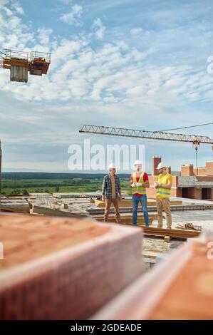 Three men in protective helmets standing on the building site Stock Photo
