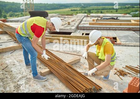 Experienced focused builders in cotton gloves selecting rebars Stock Photo