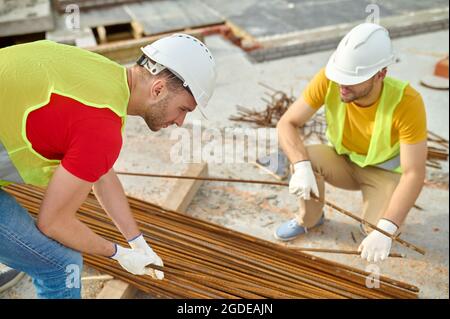 Two experienced workers in safety vests and hardhats choosing rebars Stock Photo