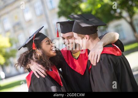 Three graduates hugging and discussing their graduation Stock Photo