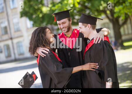 Three graduates hugging and discussing their graduation Stock Photo